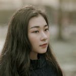 Serene outdoor portrait of a young woman with long dark hair, gazing thoughtfully.